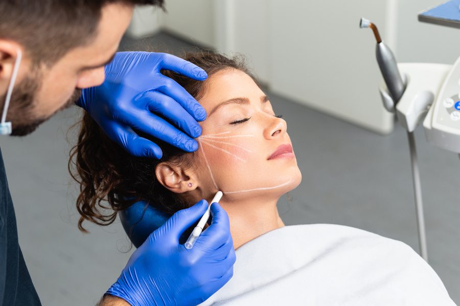 doctor's hand drawing correction lines on young woman's face for plastic surgery