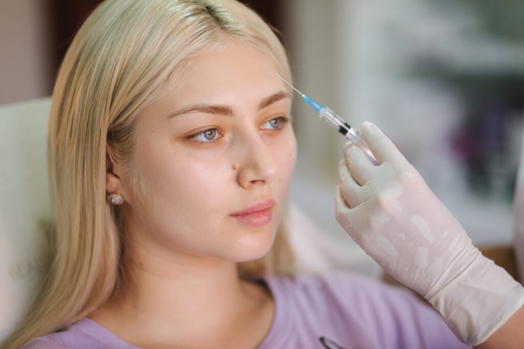 botox and dermal fillers - Hands of cosmetologist making injection in face, lips. Young woman gets beauty facial injections in medical clinic